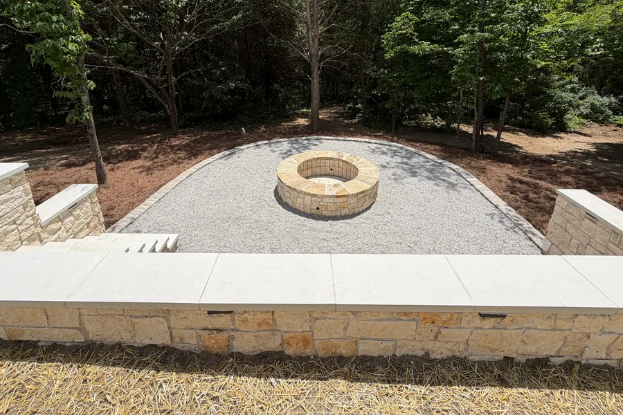 Crushed gravel court with a round stone fire pit, framed by stone block walls and steps