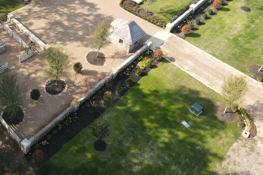 Aerial view of new planting beds with shrubs along a stone wall, young trees in mulch rings and a fresh green lawn